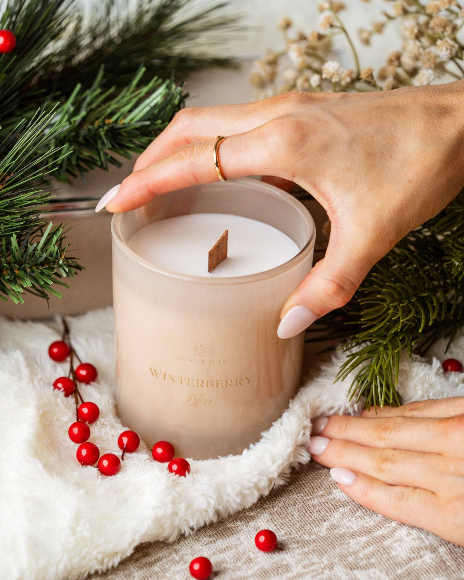 hand holding the Winterberry Bliss Candle surrounded by cranberries and balsam fir