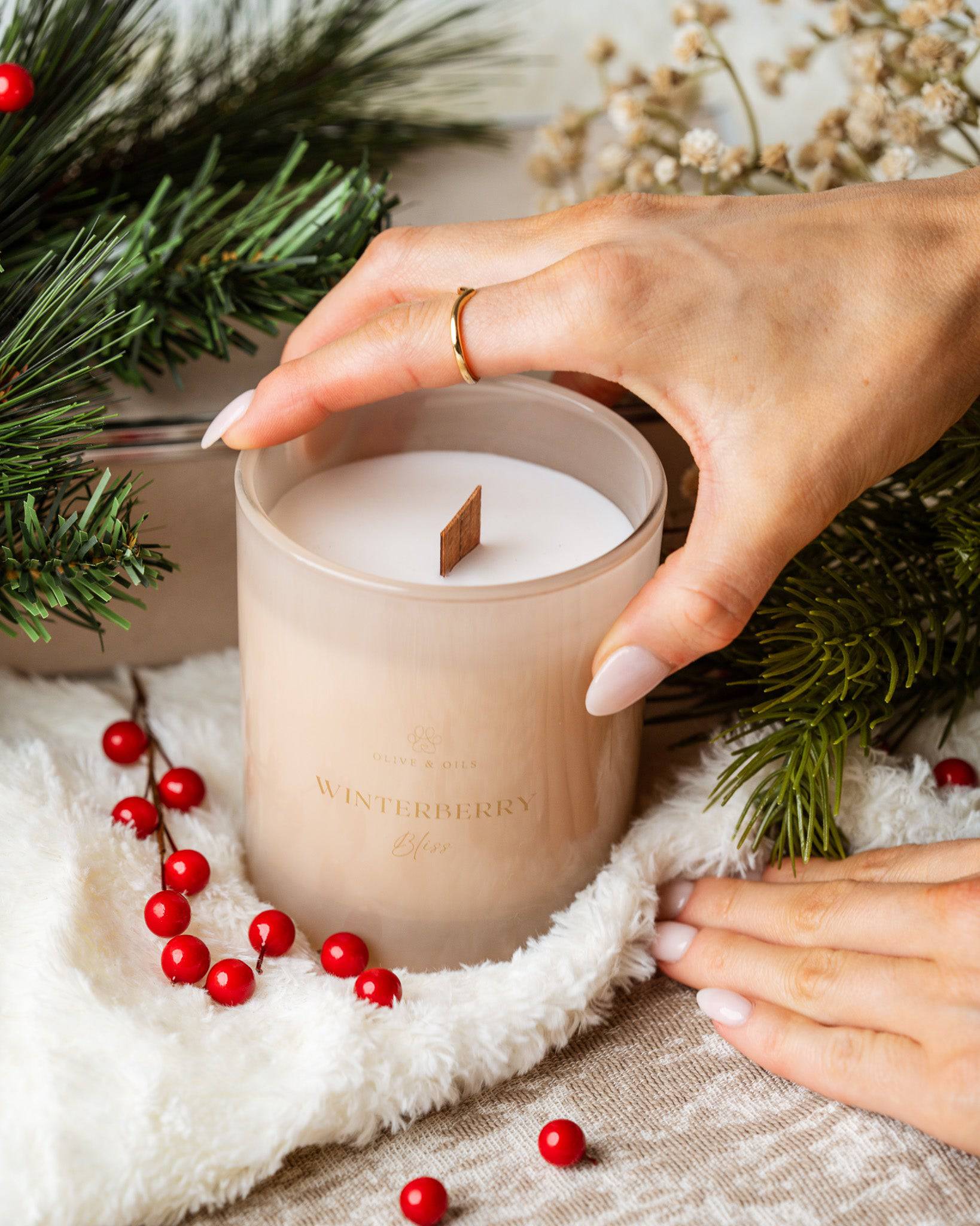 hand holding the Winterberry Bliss Candle surrounded by cranberries and balsam fir